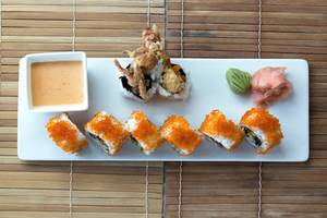 Ein weißes Tablett mit verschiedenen Sushi-Rollen und einer kleinen Schüssel Sauce auf einer Bambusmatte.