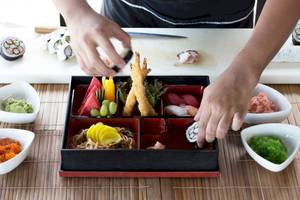 Ein Sushi-Teller ist auf einem Tisch mit verschiedenen Gerichten und Zutaten vorbereitet.