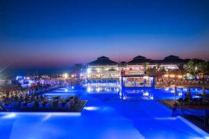Abendansicht des Poolbereichs des Club Nena Hotels mit beleuchtetem Wasser und Gästebereichen.