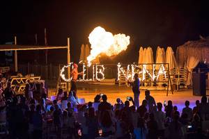 Feuershow mit Schriftzug Club Nena bei Nacht im Freien vor einer tanzenden Menge.