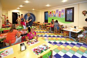 Club Nena Kinderfrühstücksbereich mit bunten Tischdecken und Wandmalerei.
