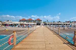 Club Nena Hotel am Strand mit vielen Gästen, Liegestühlen und Schirmen.