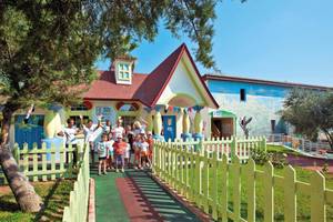 Gruppe von Kindern und Erwachsenen im Club Nena Kinderclub vor einem bunten Gebäude.