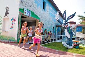 Kinder laufen vor einem Gebäude mit einer riesigen Bugs-Bunny-Figur und einer bunten Wandmalerei