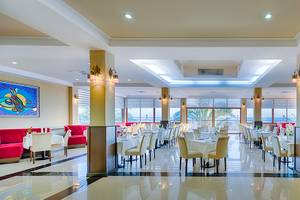 Innenansicht des Restaurants im Club Nena Hotel mit gedeckten Tischen und Stühlen, großen Fenstern und Kunstwerken an der Wand.