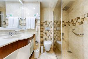 Badezimmer im Club Nena Hotel mit gefliester Wand, Dusche, Toilette und Waschbecken.