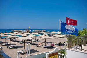 Strand des Club Nena Hotels mit Sonnenschirmen, Liegen und Flaggen