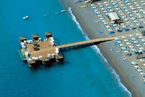 Luftaufnahme des Club Nena Hotels mit Außenbereich am Strand, vielen Sonnenschirmen und einem Steg zum Wasser.