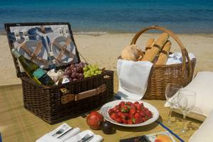 Picknickkorb mit Früchten, Brot und Wein am Strand vor dem Mykonos Grand Hotel & Resort.