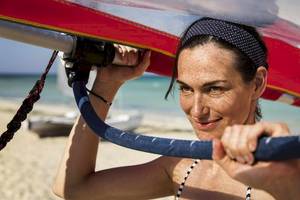Frau auf dem Strand mit einem Segelboot, das sie in die Luft hebt.