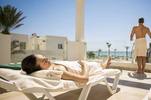Eine Frau entspannt sich auf einem Liegestuhl auf dem Balkon des Robinson Djerba Bahiya Hotels mit Blick auf das Meer.