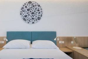 Ein Hotelzimmer im Osmine Slano mit einem Bett, zwei weißen Kissen, einem blauen Kopfteil und einer Wanddekoration.