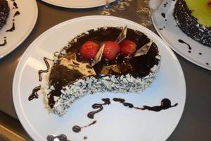 Ein Stück Schokoladenkuchen mit Erdbeeren auf einem weißen Teller mit Schokoladensauce.