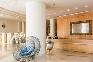 Lobby des Ikos Oceania Hotels mit Rezeption, Holzwänden und Sitzmöbeln.