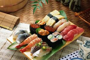 Eine Vielzahl von Sushi auf einem gelben Teller, der auf einem grünen Palmblatt liegt.