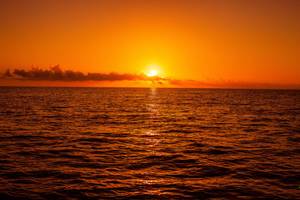 Sonnenuntergang über dem Meer mit reflektierenden Lichtern auf der Wasseroberfläche.