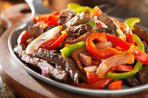 Eine Platte mit Fajitas, bestehend aus Fleisch, Paprika und Zwiebeln, serviert auf einem runden Teller.