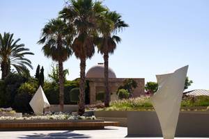 Außenbereich des Rhodes Bay Hotel & Spa mit weißen Skulpturen und hohen Palmen.