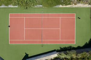 Luftaufnahme des Tennisplatzes im Rhodes Bay Hotel & Spa mit zwei Spielern auf grünem und rotem Boden.