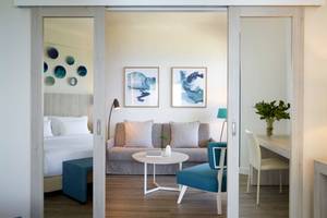Inneneinrichtung von einem Doppelzimmer im Rhodes Bay Hotel & Spa mit einem Bett, Sofa, Tisch, Stuhl und Lampe.