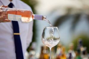 Mitarbeiter des Rhodes Bay Hotel & Spa gießt rosa Wein in ein Glas