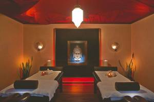 Massageraum im Rhodes Bay Hotel & Spa mit zwei Massagebetten, roten Akzenten und einem Buddha-Bild.