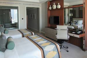 Innenansicht eines Hotelzimmers im Taj Dubai mit zwei Betten, Schreibtisch und Fernseher.