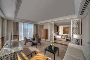 Hotelzimmer im Taj Dubai mit Schlafzimmer, Wohnzimmer, Tisch und Fernseher.