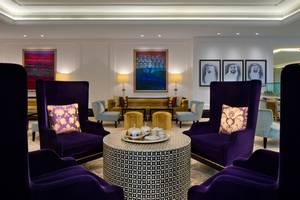 Loungebereich im Taj Dubai Hotel mit violetten Sesseln, runden Tisch und Kunstwerken an der Wand.