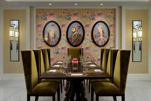 Speisesaal des Taj Dubai mit drei Porträts an der Wand, gedeckter Tisch mit Wein und Kerzen.