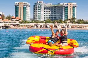 Zwei Personen auf einem gelben und roten Schlauchboot im Wasser vor dem Sherwood Exclusive Lara Hotel.