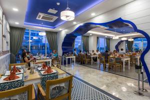Restaurant im Sherwood Exclusive Lara Hotel mit blauen Akzenten und Gästen, die an Tischen sitzen.