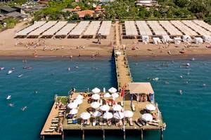 Luftaufnahme des Sherwood Exclusive Lara Hotels mit Strand und vielen Gästen, die schwimmen und sonnenbaden.