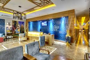 Lobby des Sherwood Exclusive Lara Hotels mit blauen Wänden, goldenem Vasen, Sitzbereich und Fernseher.