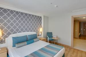 Innenansicht eines Schlafzimmers im Sherwood Exclusive Lara Hotel mit Bett, Nachttischen und offenem Tür.