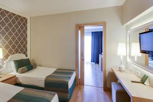 Innenansicht eines Doppelzimmers im Sherwood Exclusive Lara Hotel mit zwei Betten, Dekor, Lampen und Fernseher.