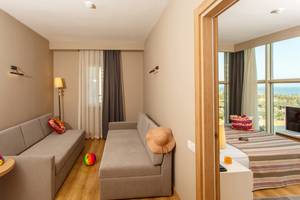 Innenansicht eines Zimmers im Sherwood Exclusive Lara Hotel mit zwei Sofas, einem Tisch, Spielzeug und einem Blick auf das Meer.