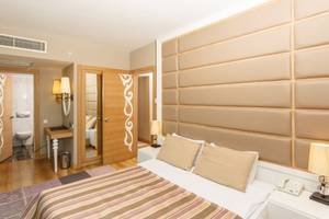 Hotelzimmer im Sherwood Exclusive Lara mit Doppelbett, Kissen, Nachttischen und cremefarbenen Wänden.