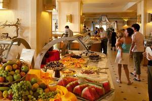 Buffet im Hotel Creta Star mit verschiedenen Desserts, Obst und Menschen, die essen.
