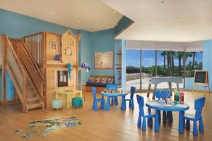 Spielzimmer im JA Palm Tree Court Hotel mit bunten Möbeln, Holztreppe und Puzzle auf dem Boden.