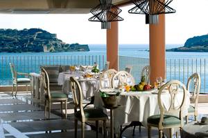 Terrasse mit Meerblick im Domes of Elounda, Autograph Collection mit gedeckten Tischen und Früchten.
