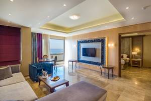 Innenansicht eines Zimmers im Adams Beach Hotel mit Wohnzimmer, Essbereich, Fernseher und Blick auf das Meer.