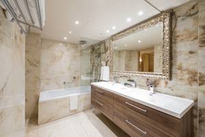 Ein elegantes Badezimmer im Adams Beach Hotel mit Marmorwänden, Badewanne und Doppelwaschbecken.
