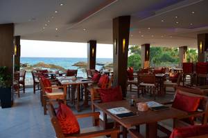 Innenansicht des Restaurants im Adams Beach Hotel mit Blick auf das Meer und Sonnenschirme.