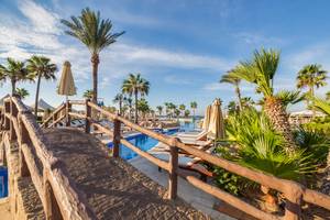 Poolbereich des Adams Beach Hotels mit Sonnenliegen und Palmen