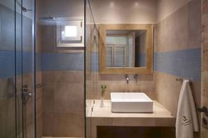 Badezimmer im Vencia Boutique Hotel mit Glasdusche, Waschbecken und beigen Fliesen.