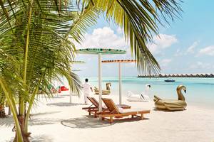 Luxuriöse Strandszene am LUX South Ari Atoll mit Palmen, Liegestühlen und Schlauchbooten