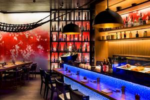 Innenansicht des Restaurants im LUX South Ari Atoll Hotel mit roten und weißen Wänden, blau beleuchteten Regalen und Theke.