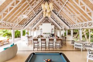 Innenansicht der Bar im LUX South Ari Atoll Hotel mit Pooltisch und hohen Holzstühlen.