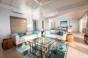 Wohnbereich des LUX South Ari Atoll Hotels mit zwei weißen Sofas, einem Glastisch und einer Glasbodenplatte.